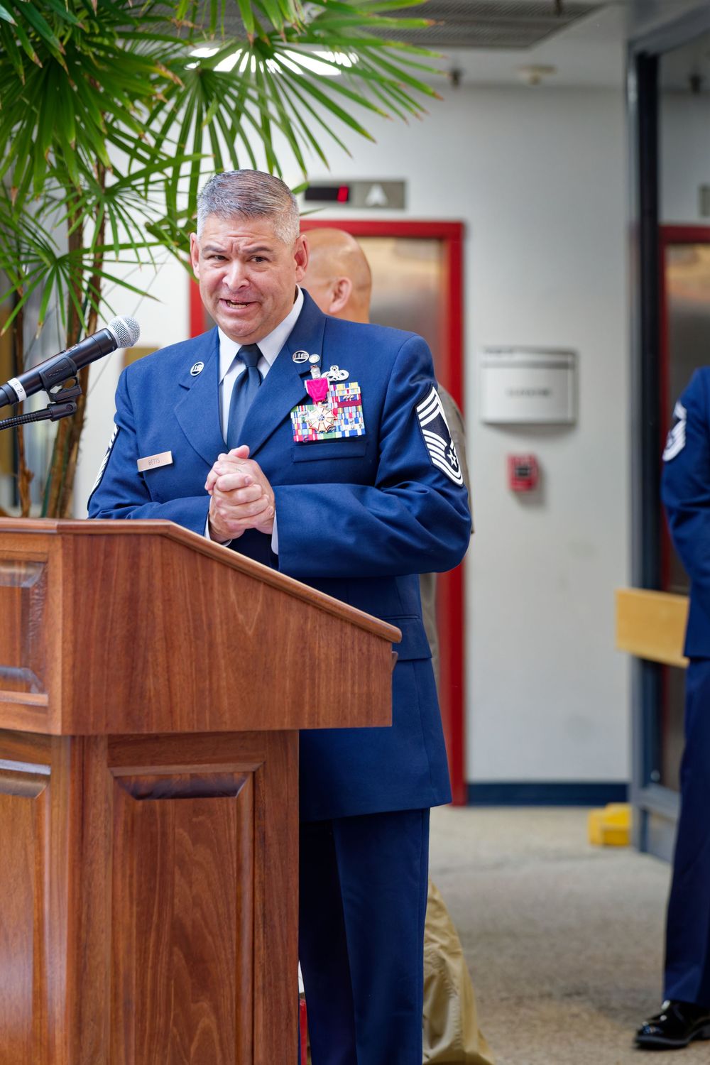 Decorated Air Force senior master sergeant delivers a speech at a wooden podium during a military event.