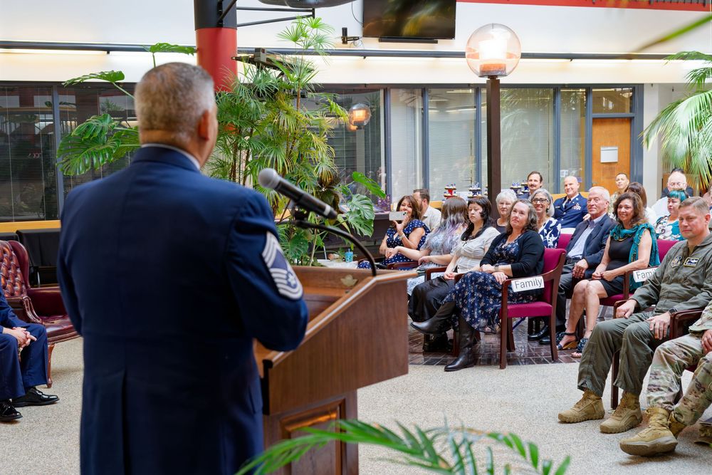 Air Force officer addresses a large seated audience during an indoor military ceremony or retirement event.