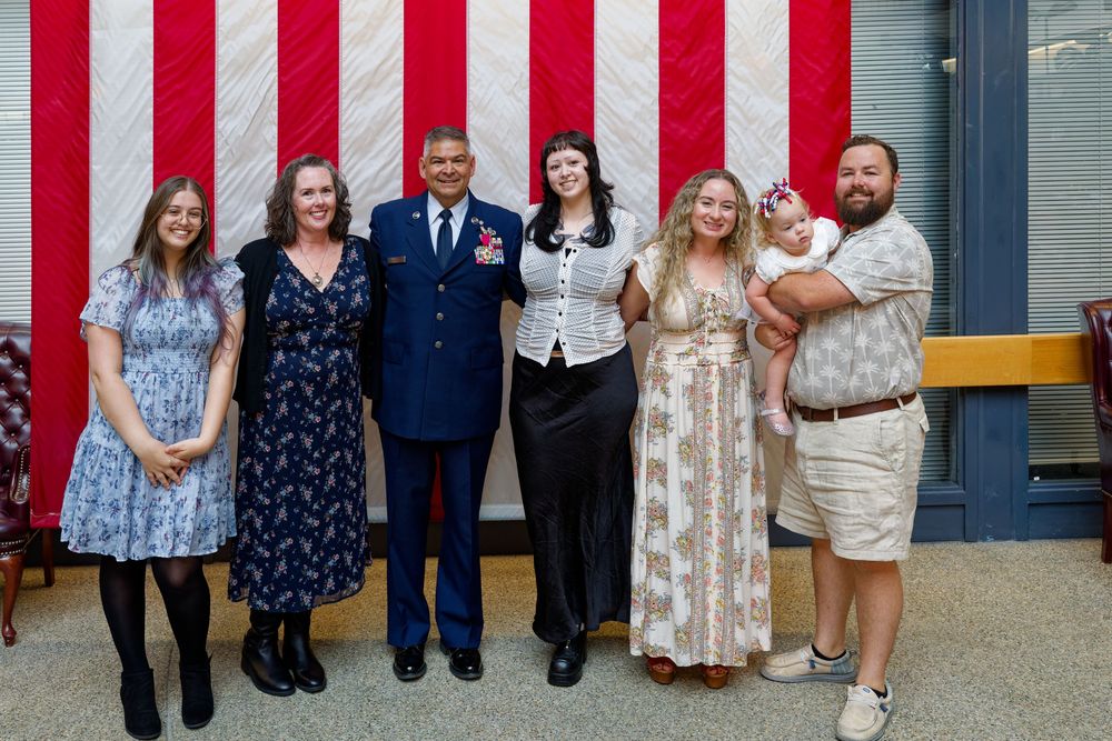 Air Force Chief Master Sergeant poses with family in front of an American flag after ceremony.
