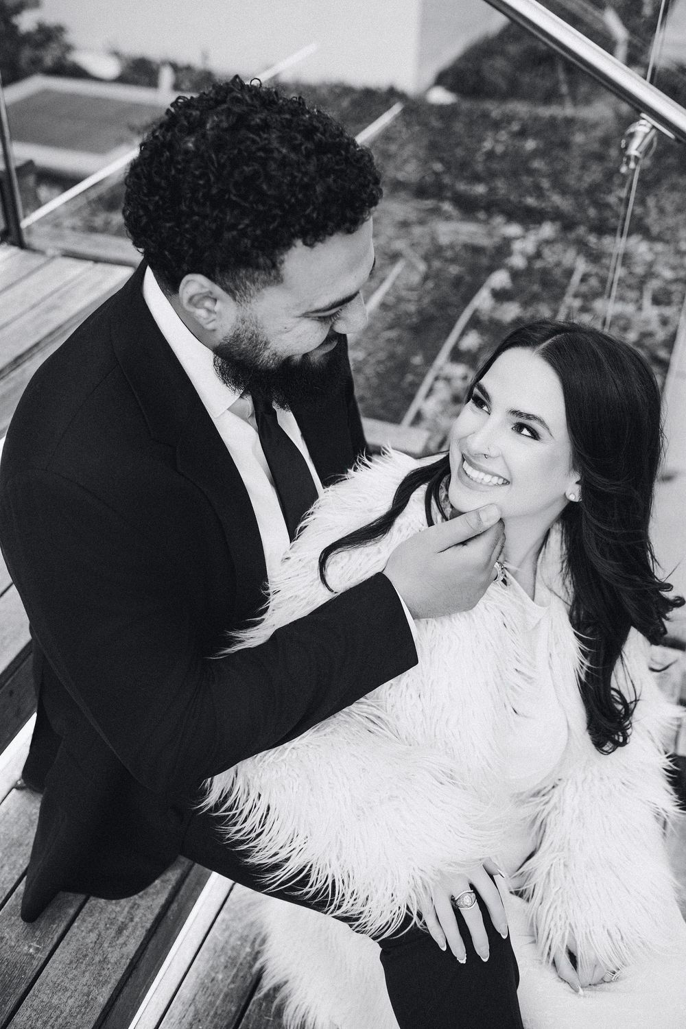 Black and white photo of a couple in formal wear sharing a romantic moment on outdoor stairs.