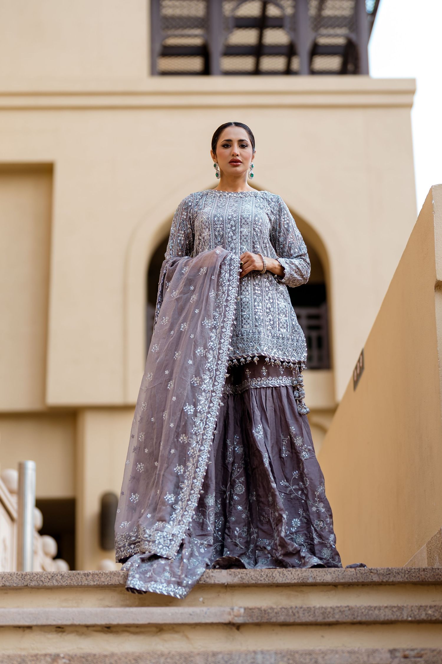 Fashion model in an embroidered gown standing on stone steps in Dubai, editorial photoshoot