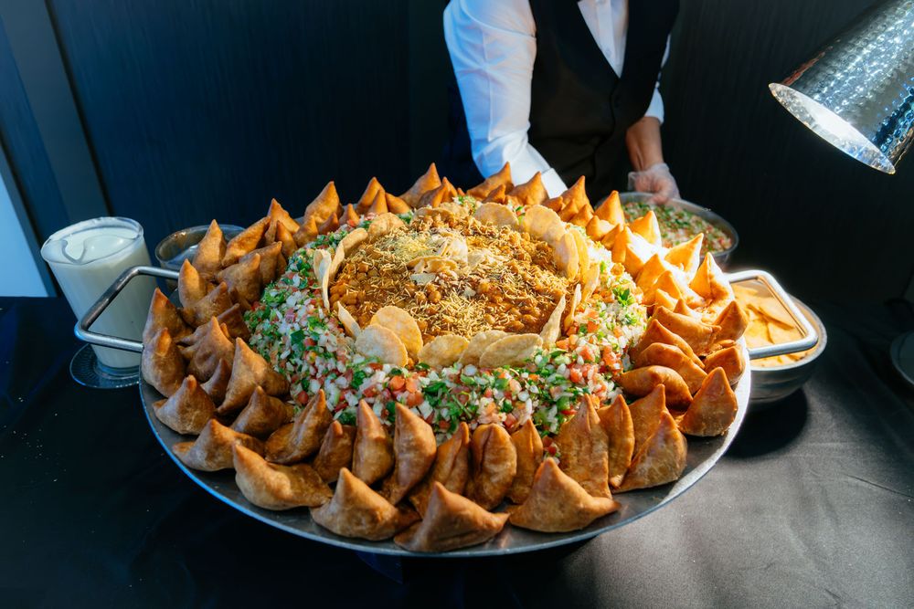 Large platter of golden fried samosas arranged around a central pile of rice topped with fresh herbs, served at a catered buffet.