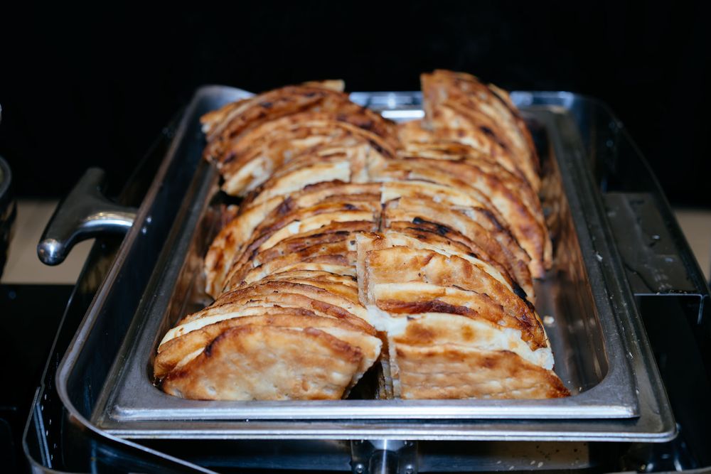 Golden-brown baked empanadas arranged in neat rows on a stainless steel chafing dish at a buffet.