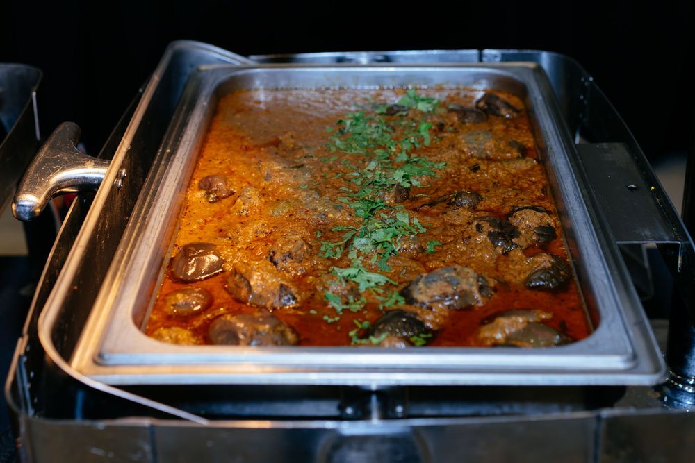 Creamy spiced meat curry garnished with fresh green herbs in a stainless steel chafing dish at a buffet.