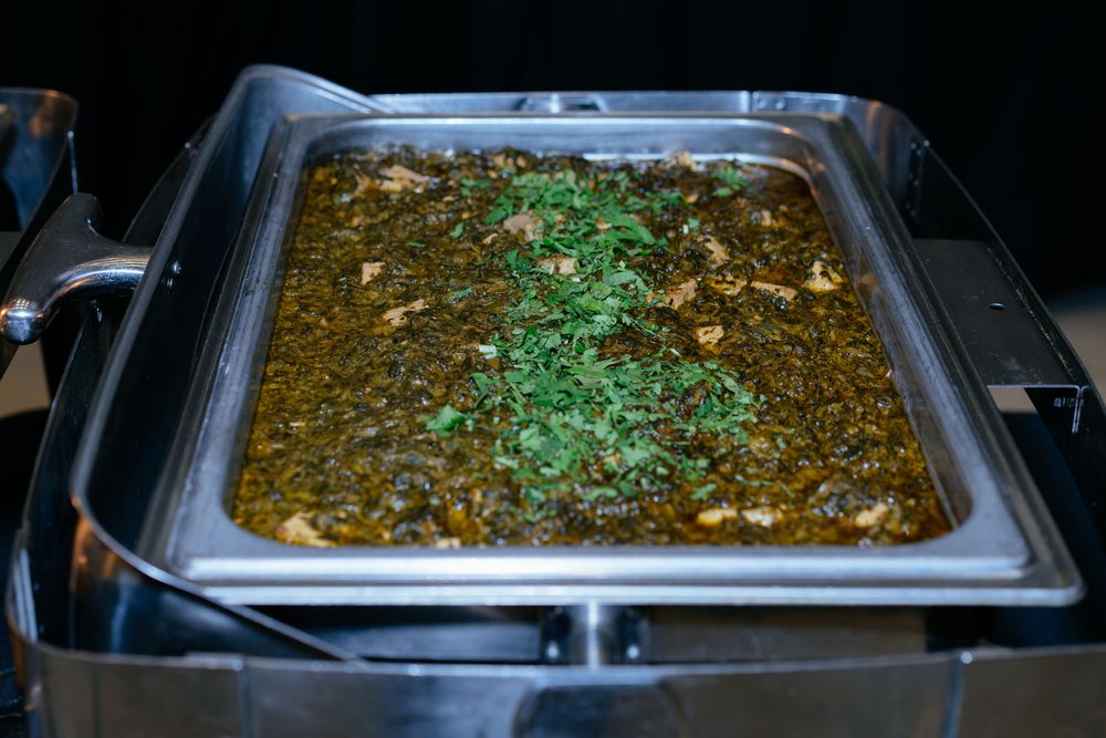 Chafing dish at a buffet filled with a creamy green spinach curry topped with fresh chopped cilantro.