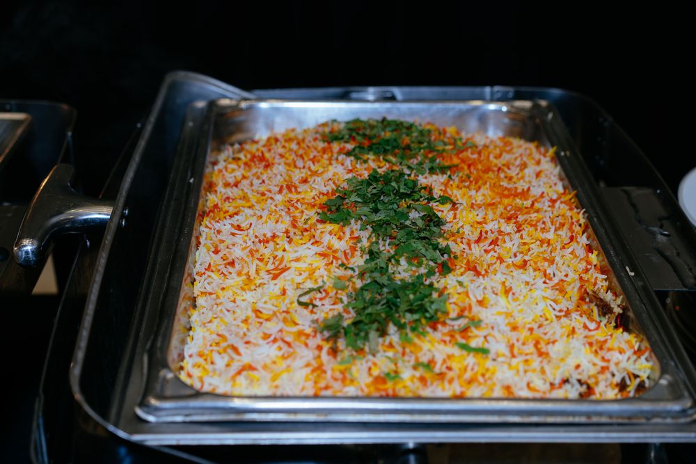 Chafing dish of fragrant saffron biryani rice garnished with fresh chopped cilantro, served at a buffet.
