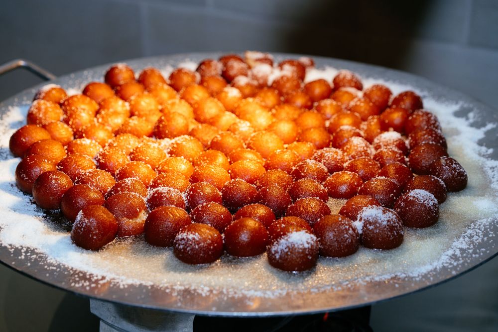 Pile of golden-brown fried dough balls dusted with powdered sugar, served on a large metal tray.