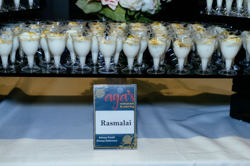 Rasmalai dessert served in small stemmed glasses on a buffet table beside a placard from Aaga's Restaurant & Catering.