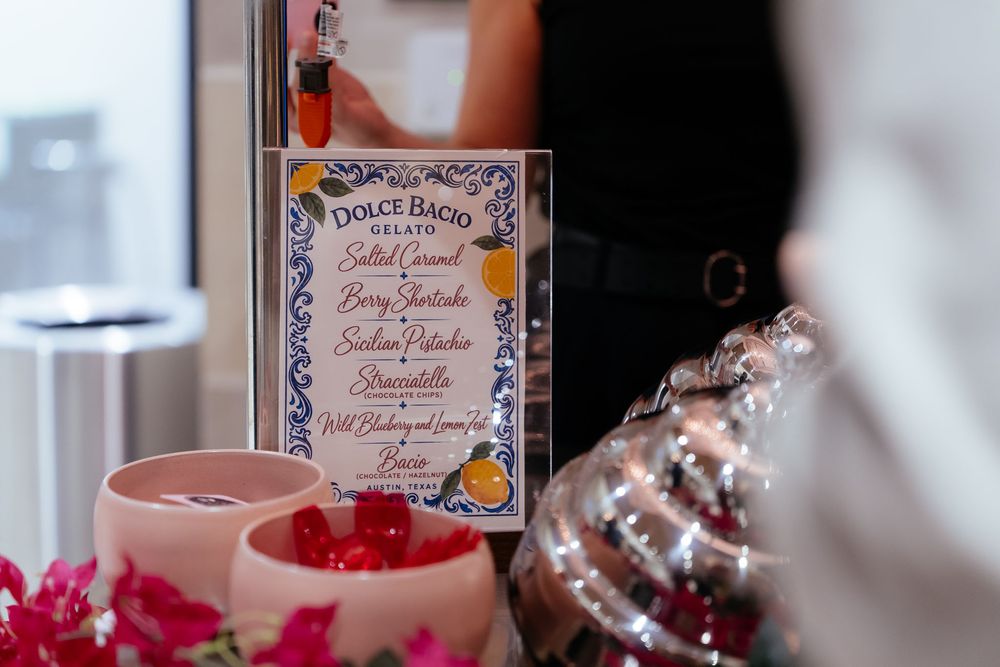 Dolce Bacio gelato menu board listing flavors like salted caramel and sicilian pistachio, beside bowls of red flower petals.