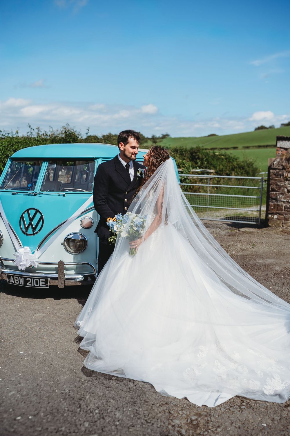 Bride and groom share a romantic moment beside a vintage teal VW camper van on their wedding day.