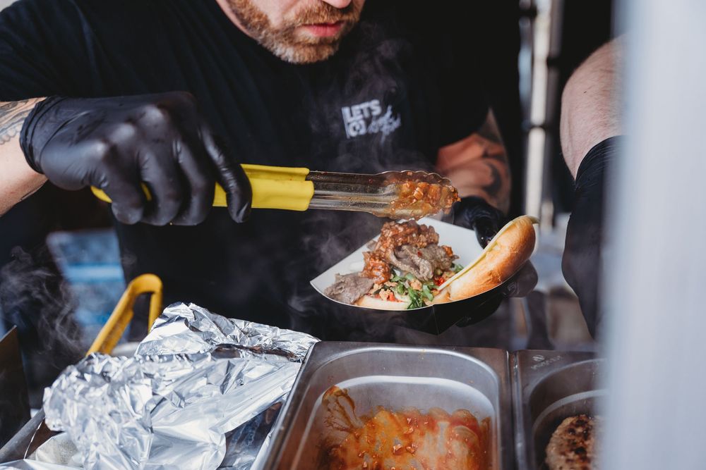 Chef in black gloves serving steaming Korean BBQ bowl with kimchi at a food truck counter.