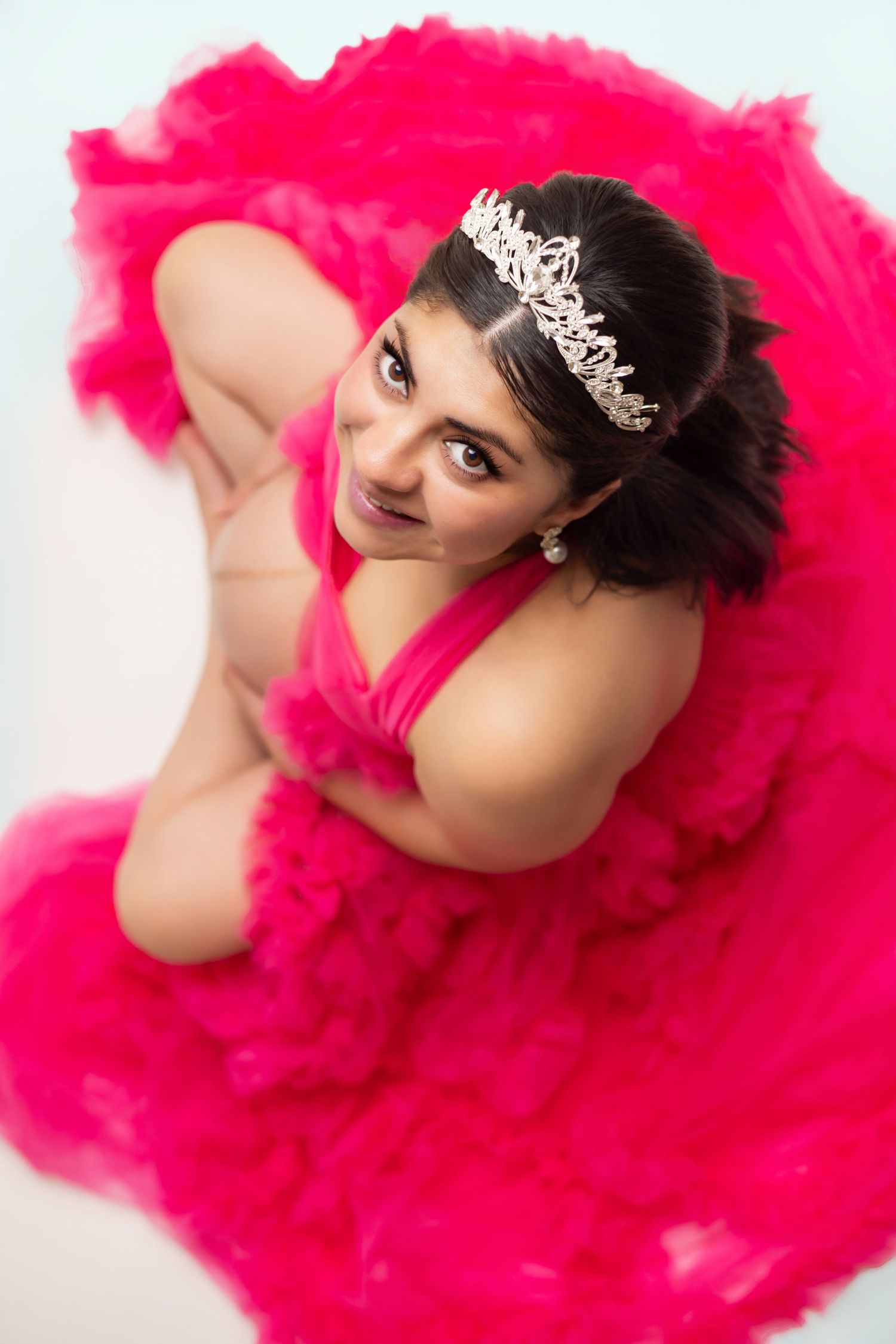 Pregnant woman and young girl in matching hot pink tulle dresses pose together in floral studio maternity photoshoot.