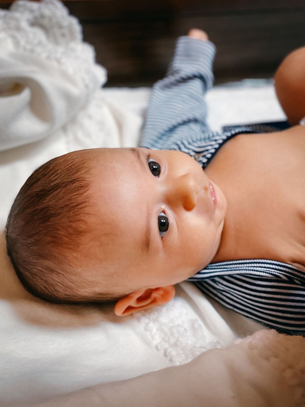 Baby boy in a christening vest looking up at the camera, Central NJ baptism photographer