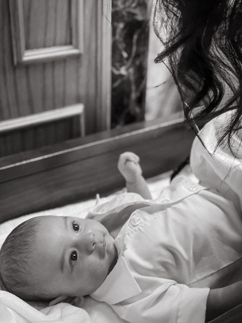 Black and white photo of a baby in a white christening outfit on a church pew, NJ baptism photography