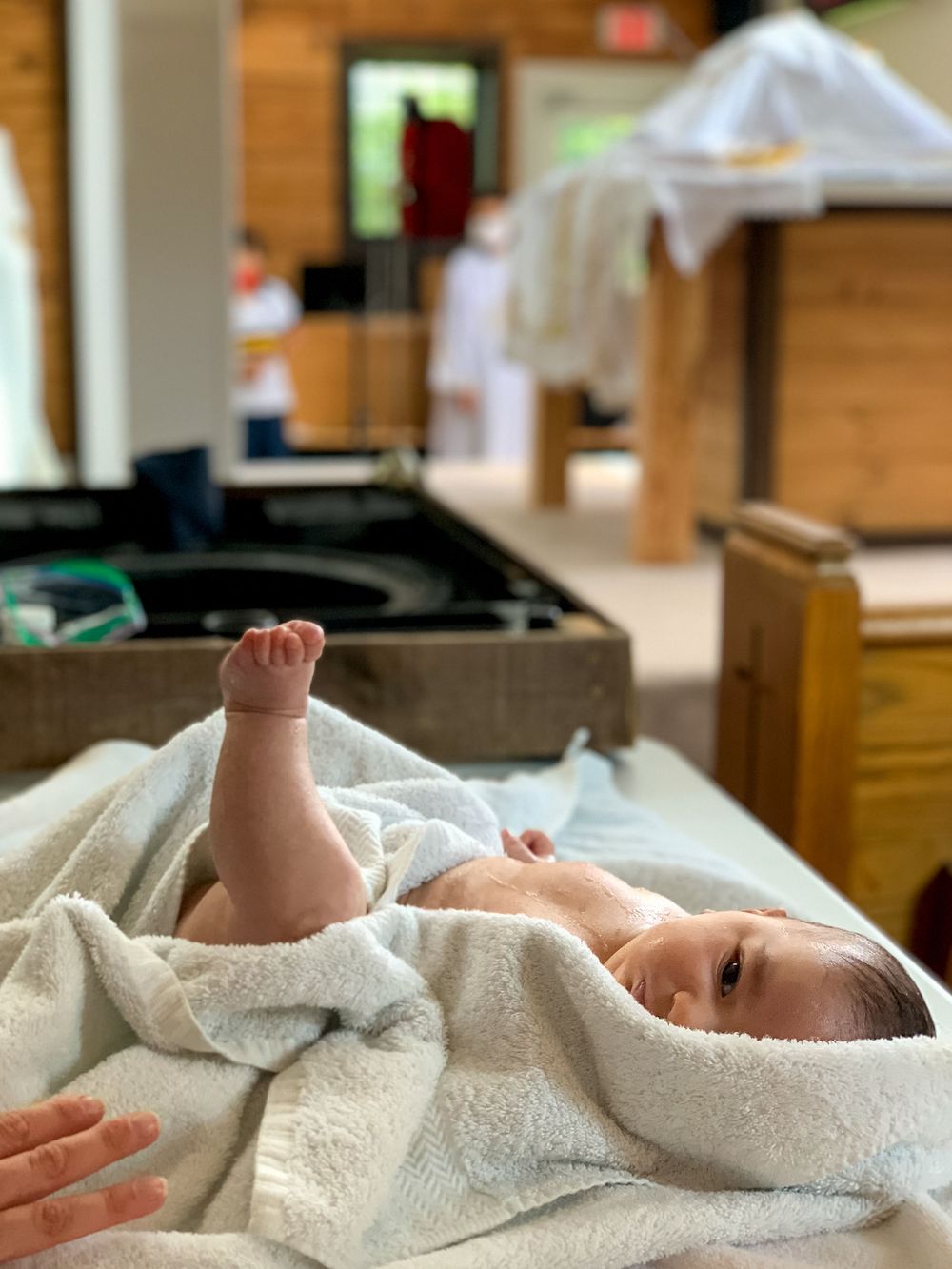 Baby wrapped in white at the baptismal font during a church baptism in Central NJ