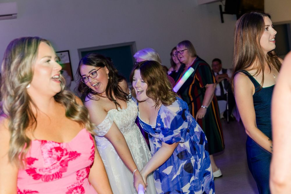 Young women in colorful dresses dancing and laughing together at a formal party or school dance event.