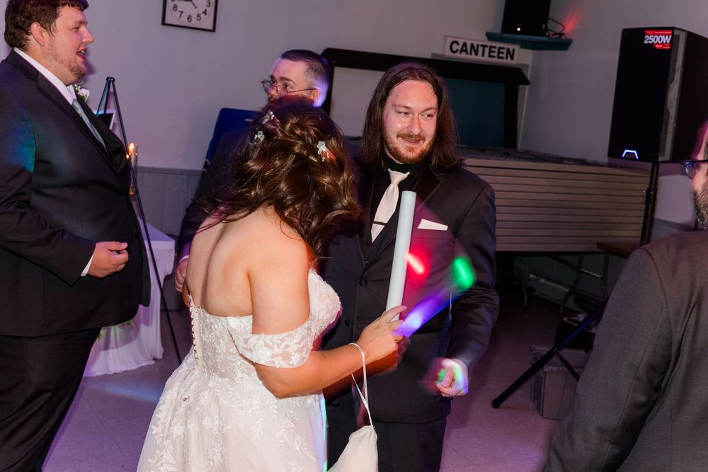 Bride and groom dancing with glow sticks at wedding reception in decorated venue.