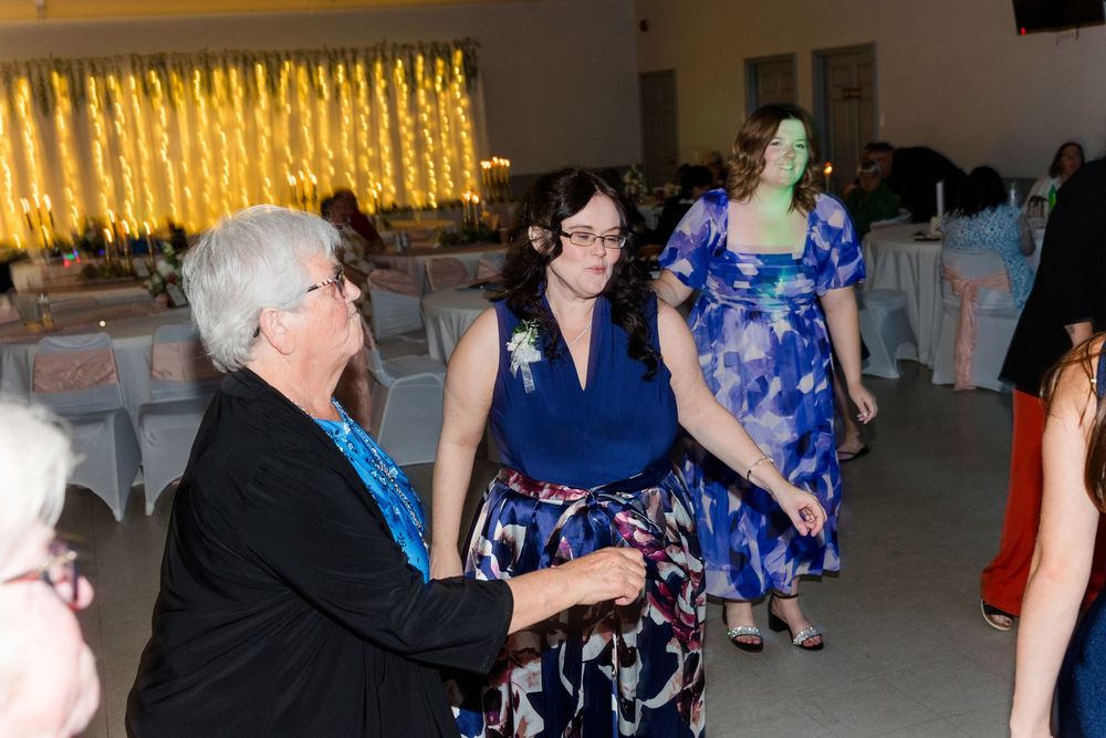 Guests enjoy lively dancing at a wedding reception in a decorated hall with string lights backdrop.