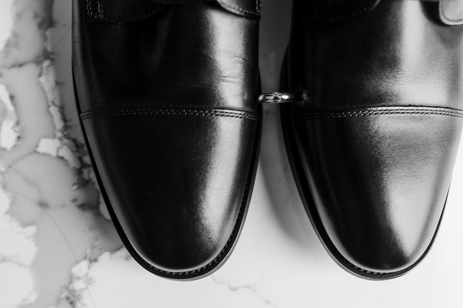 Black leather monk strap dress shoes displayed on marble surface, polished formal footwear for men.