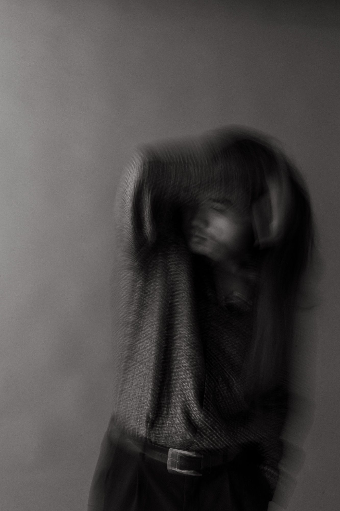 Blurred black and white portrait of a person in a knit sweater with belt, creating an eerie motion effect.