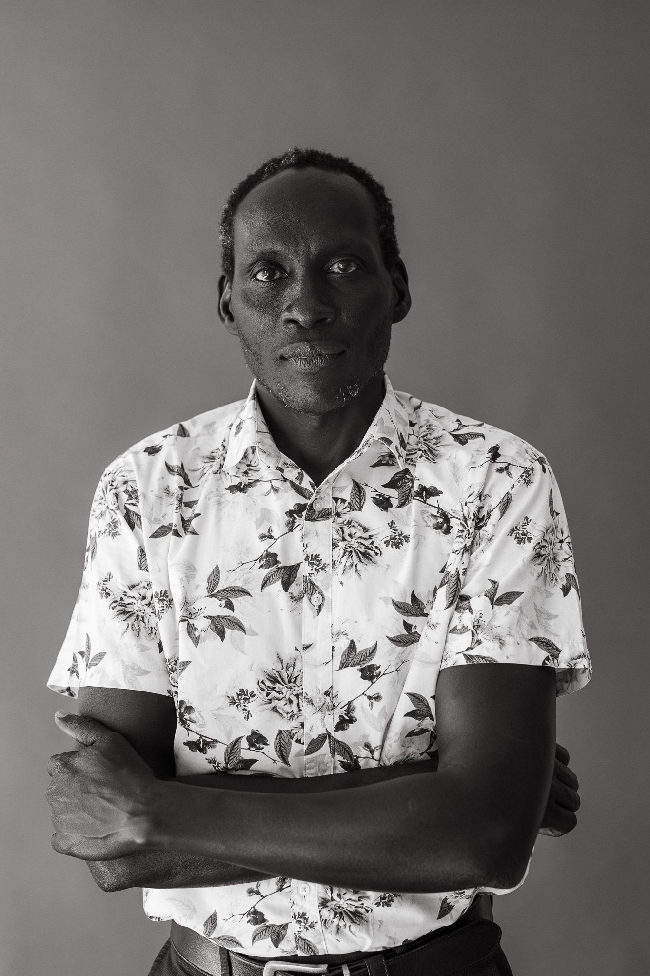 Black and white portrait of a man in floral shirt with arms crossed against gray background.