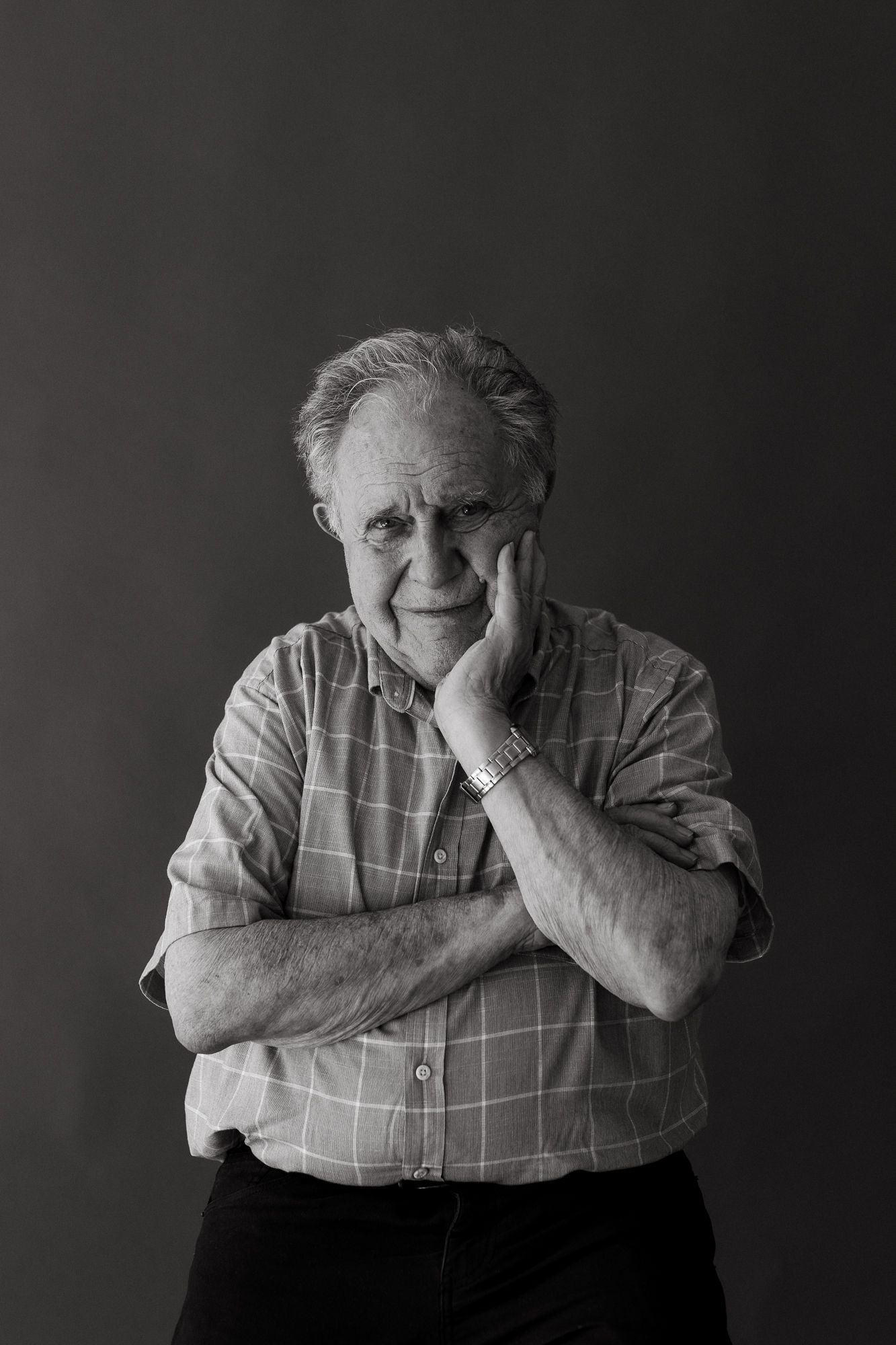 Black and white portrait of a thoughtful elderly man resting his chin on his hand with arms crossed.