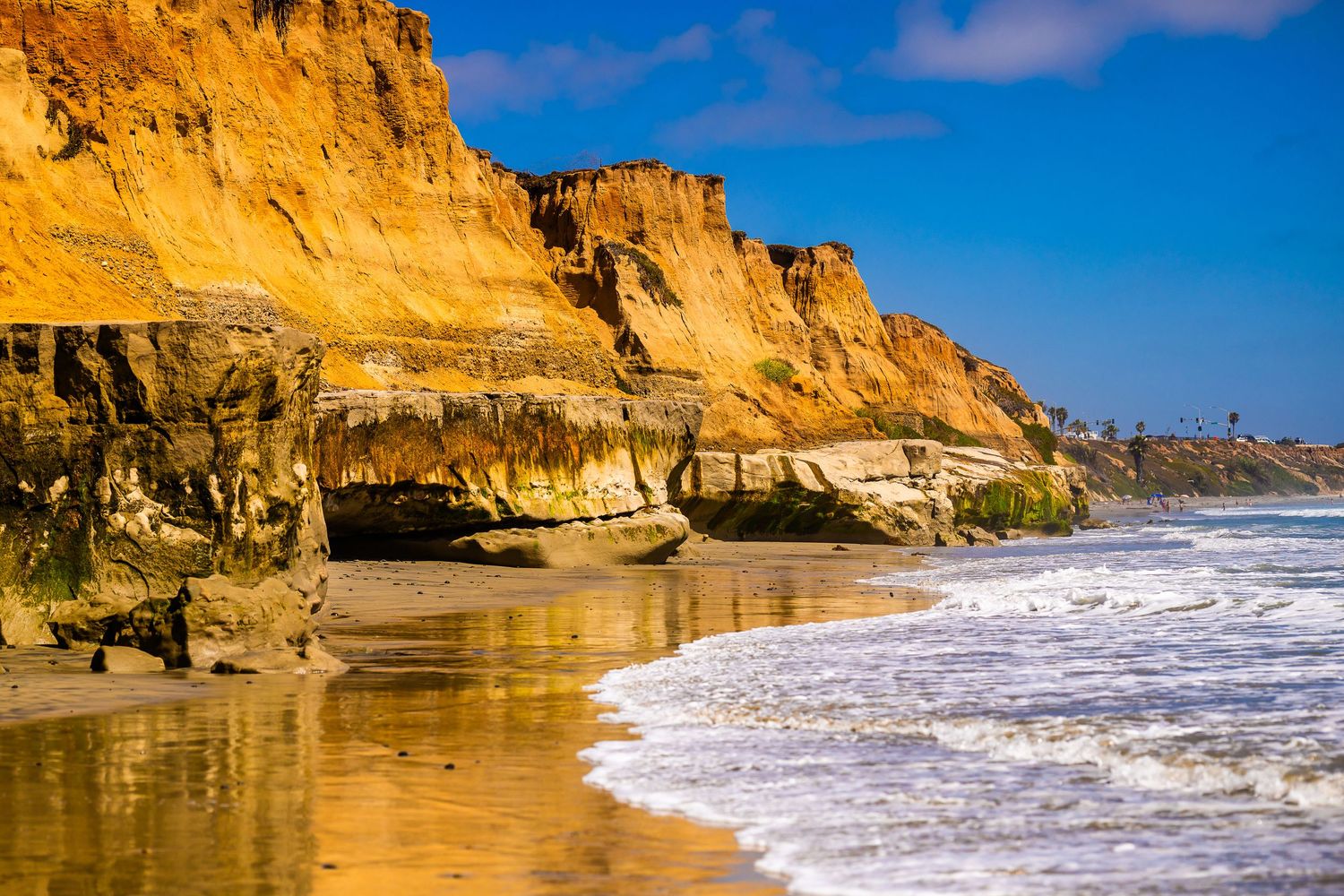 Golden sandstone cliffs tower over a sunlit beach with crashing waves in San Diego, California.