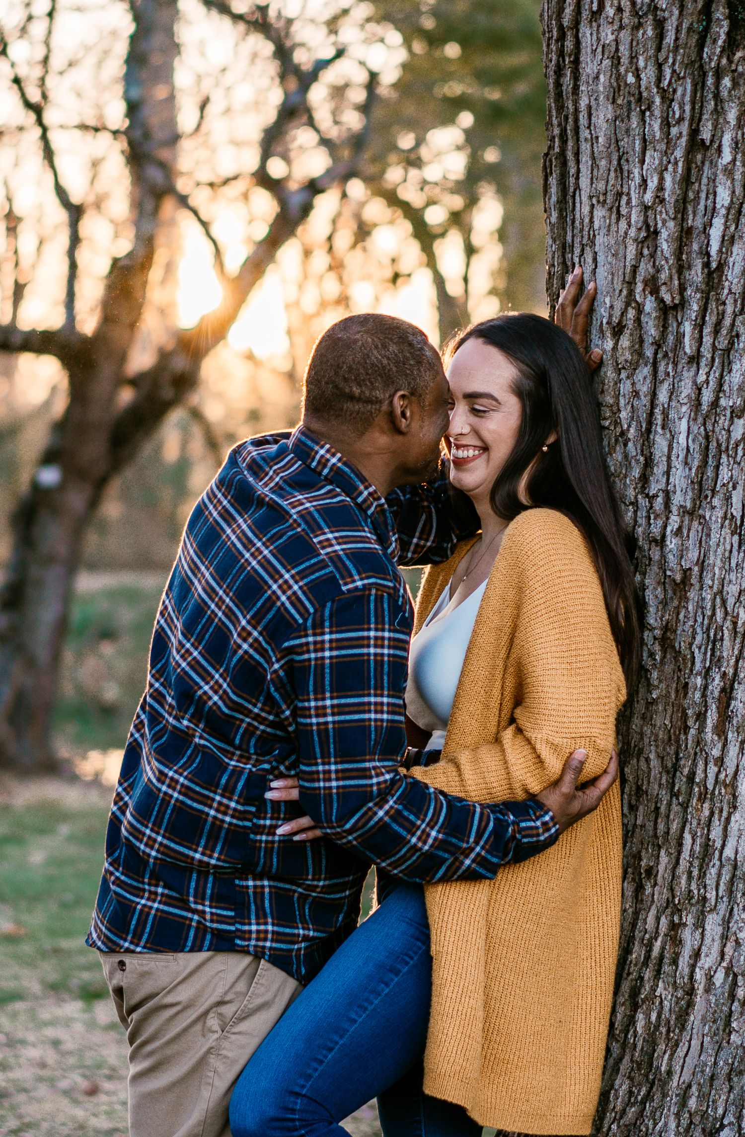 Couple sharing a romantic moment leaning against a tree at golden hour in an autumn forest setting.