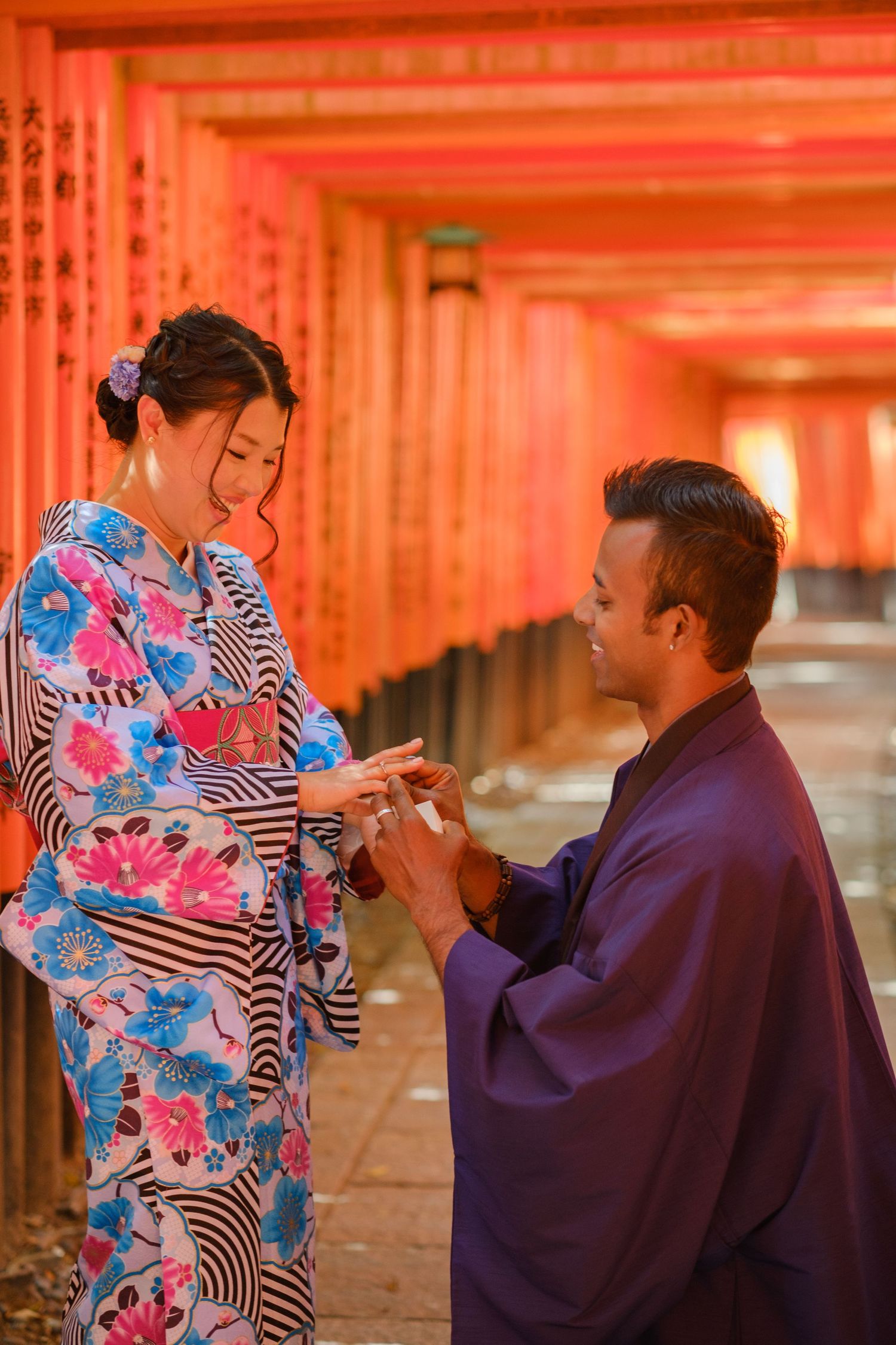 Couple in traditional kimono and robe exchange rings among the vermilion torii gates of Fushimi Inari Shrine in Kyoto, Japan.