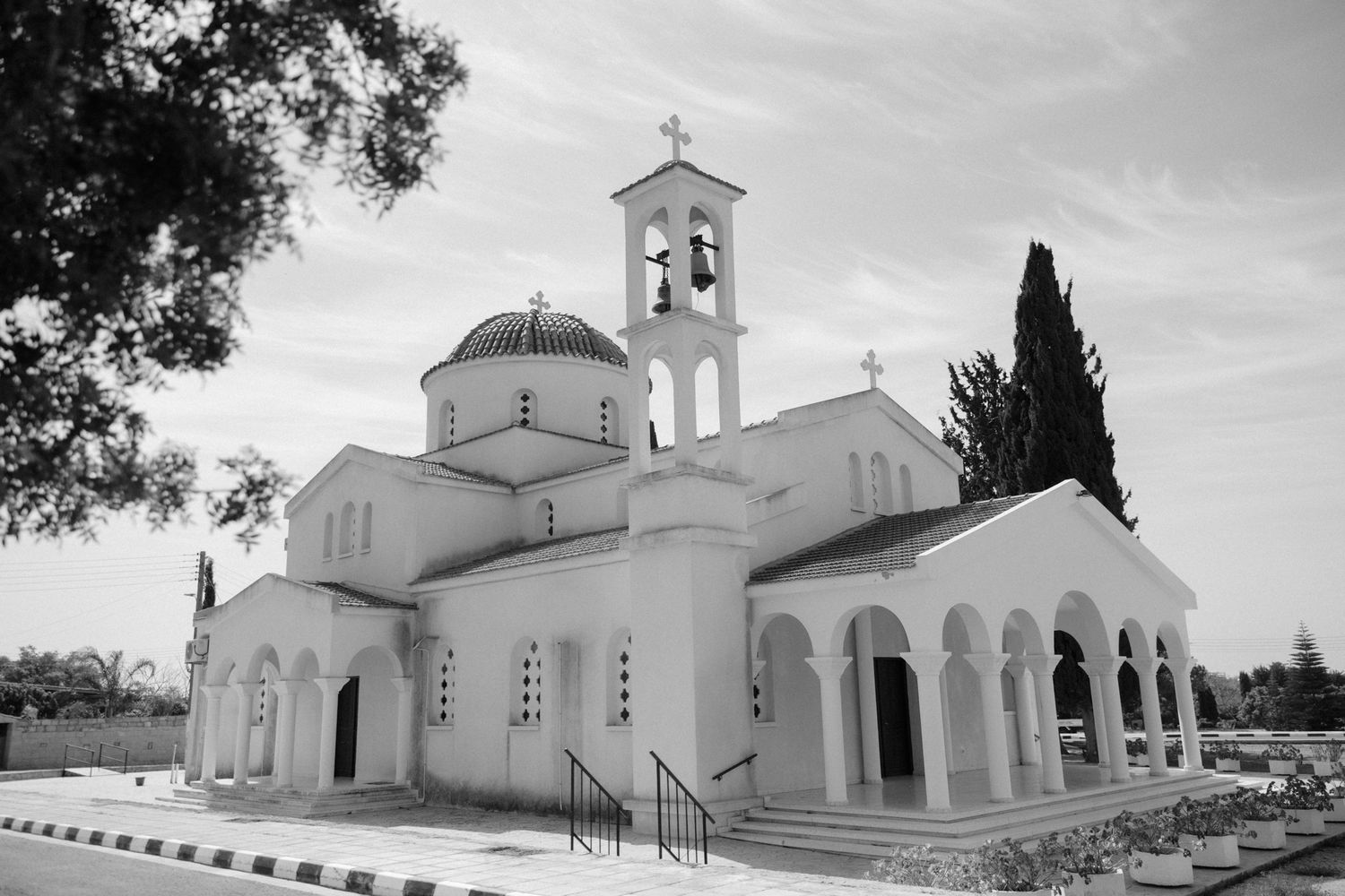 Black and white photo of a white Orthodox church with a dome, bell tower, and arched colonnade under a cloudy sky.