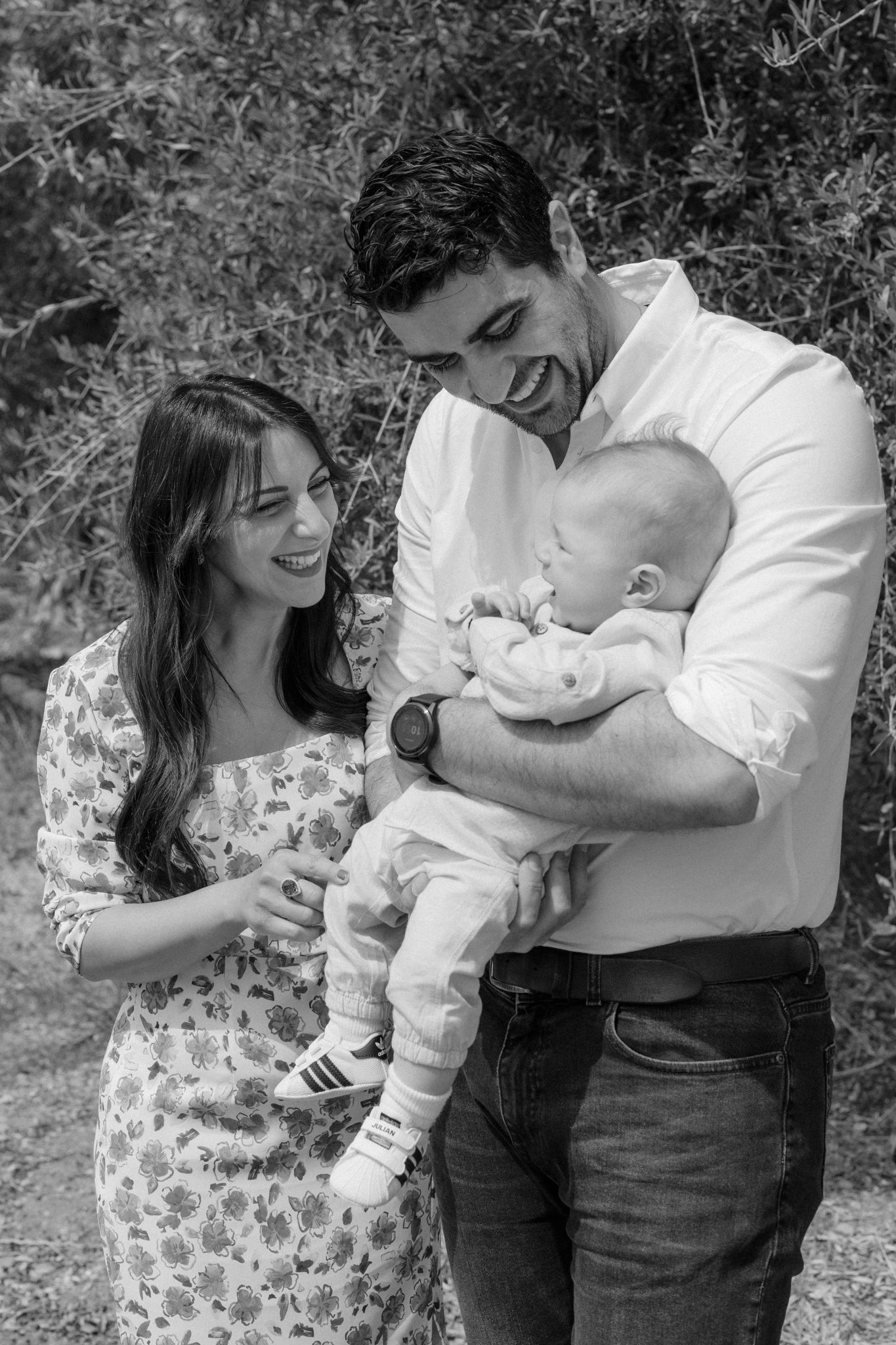 Black and white photo of a happy young family with a mother, father, and newborn baby outdoors.