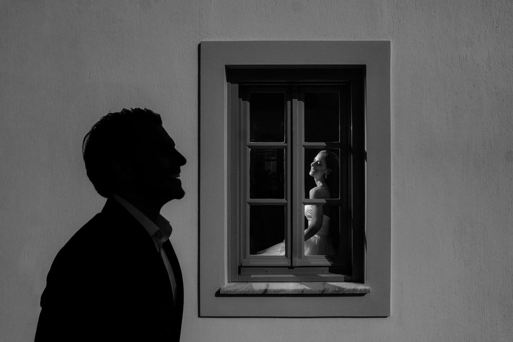 Black and white photo of a man's silhouette looking at a statue visible through a window on a textured wall.