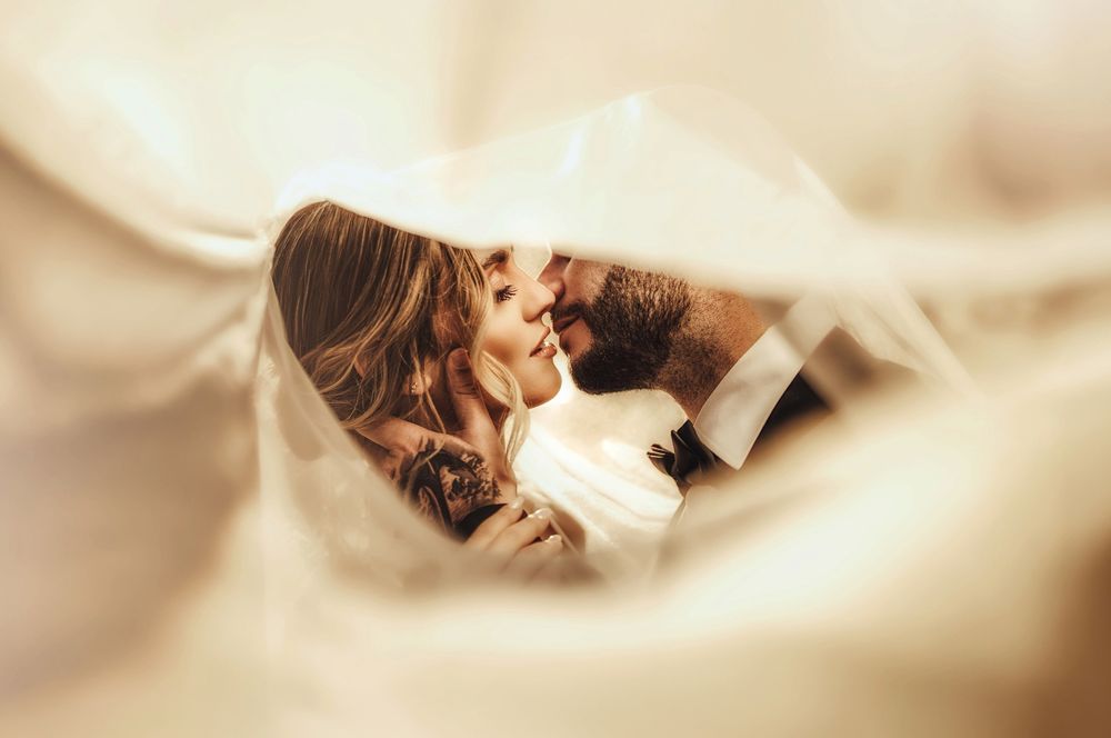 Romantic couple sharing a tender kiss under a flowing white veil on their wedding day.