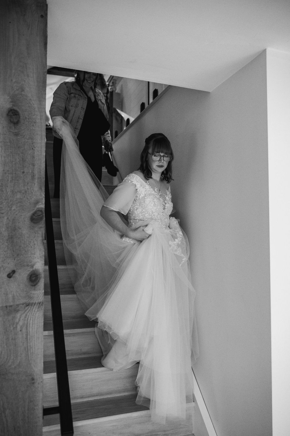 Bride in lace tulle wedding gown descending staircase in black and white photo.