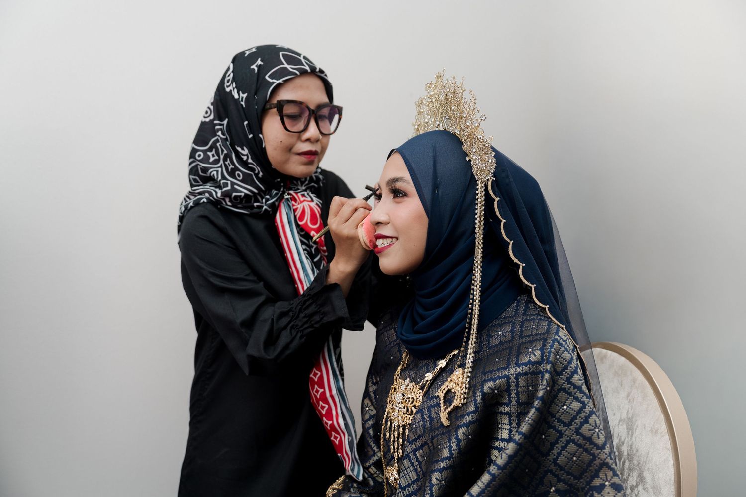 Muslim couple in traditional Javanese wedding attire sitting together at an outdoor ceremony with floral decorations and ocean view.