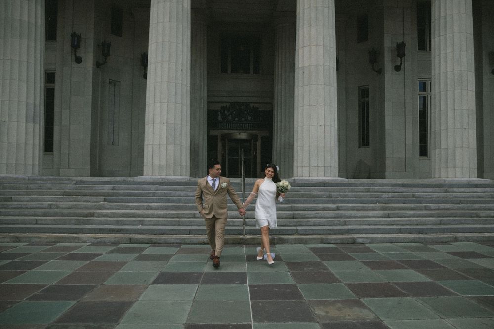 Bride and groom hold hands walking down steps of grand columned building on their wedding day.