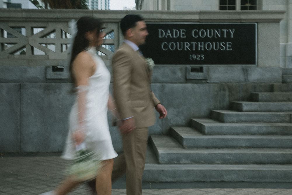 Couple walking past Dade County Courthouse 1925 sign, man in tan suit and woman in white dress.