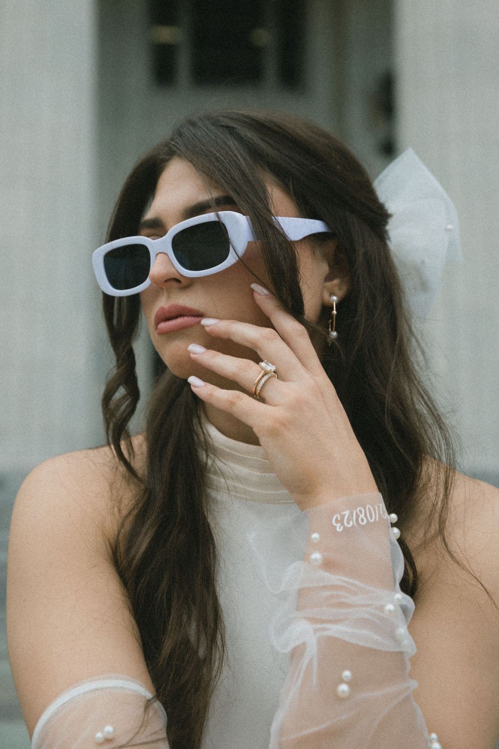 Bride wearing white square sunglasses, pearl-trimmed gloves, and a tulle bow hair accessory.