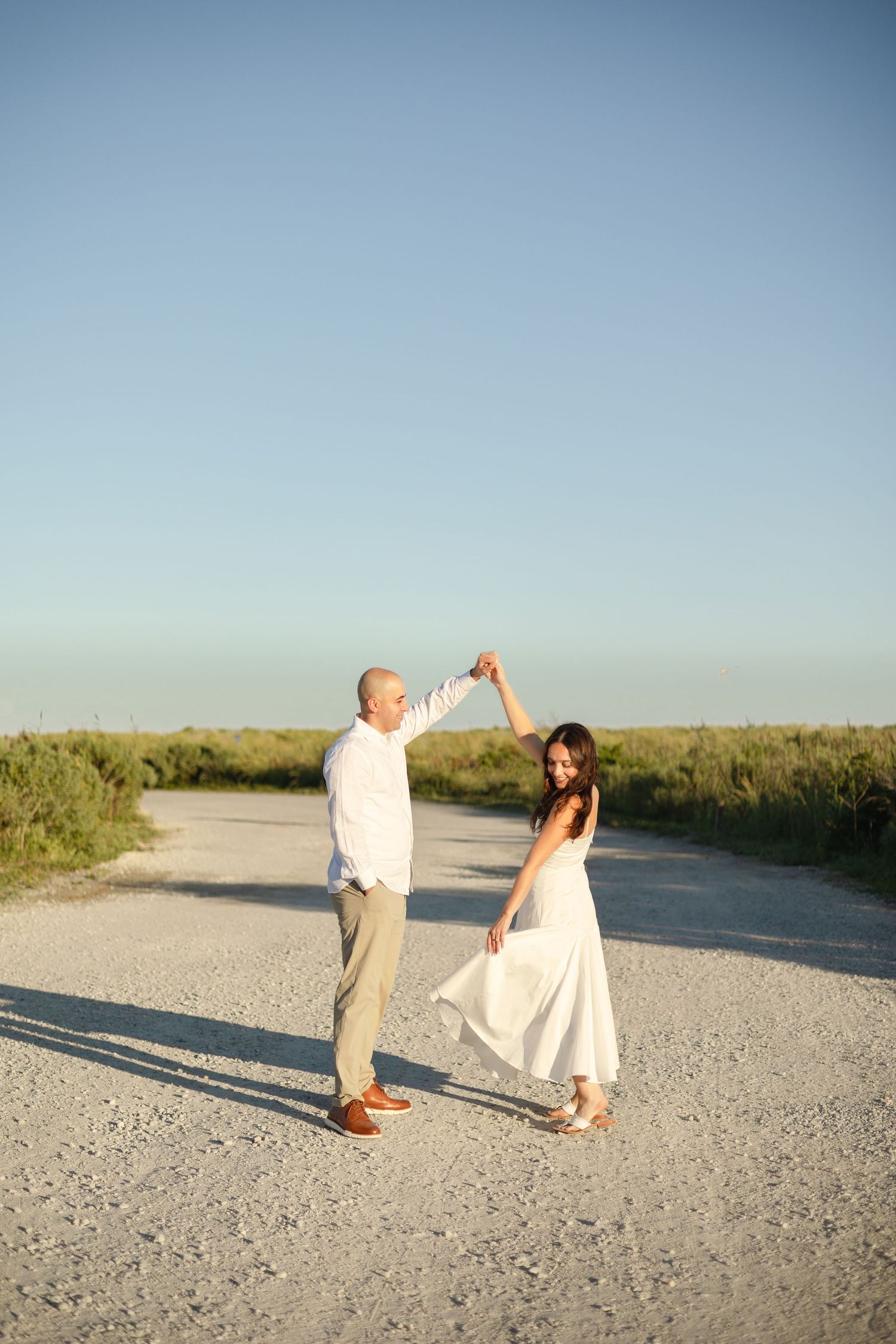 A couple embraces lovingly on a dirt path beside tall ornamental grasses on an overcast afternoon.
