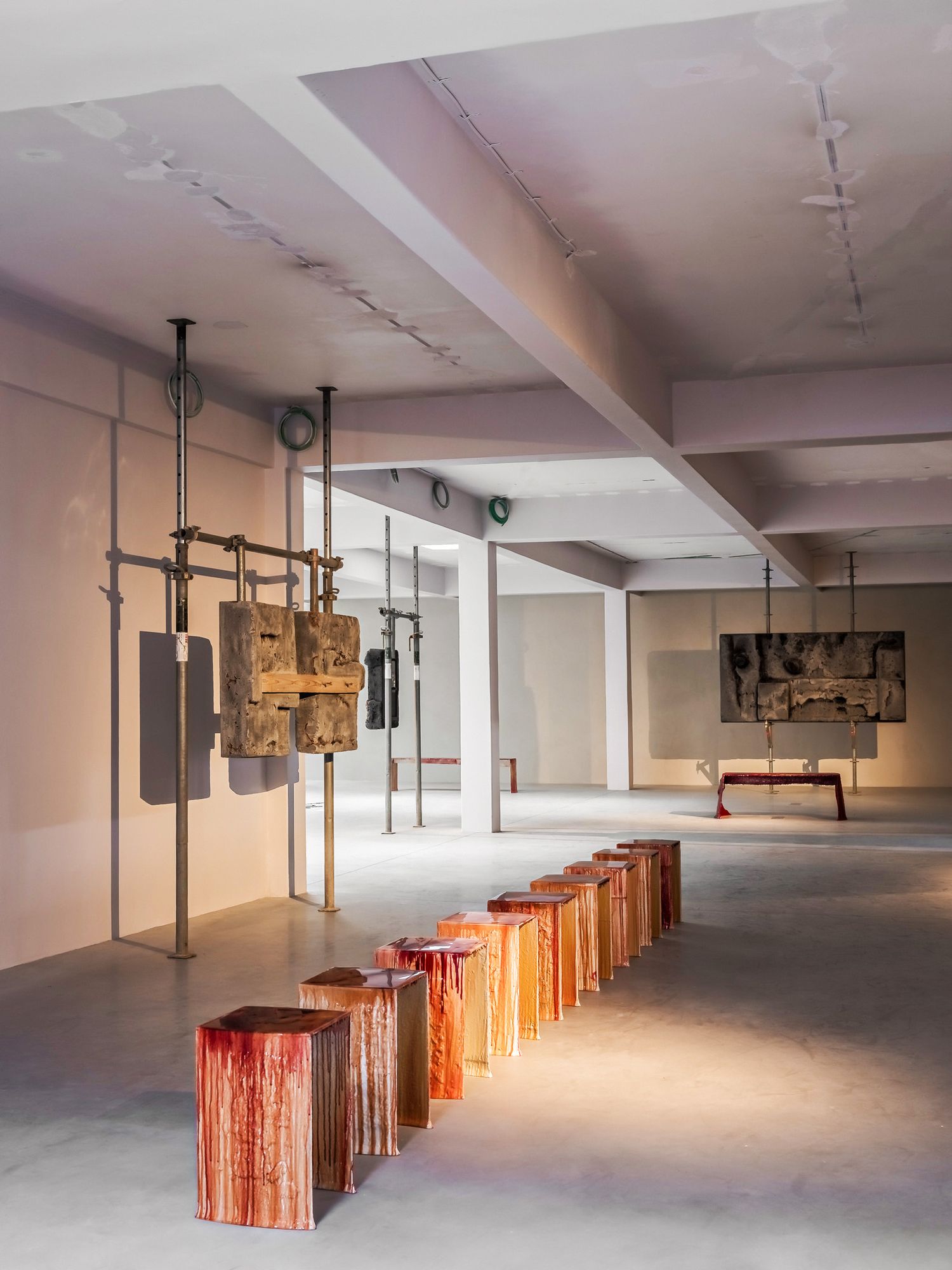 Contemporary art gallery with colorful wooden block sculptures and industrial metal installations in a spacious white room.
