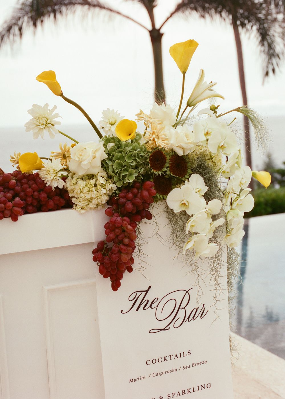 Elegant wedding bar menu cards decorated with white hydrangeas and red grapes against a light background.