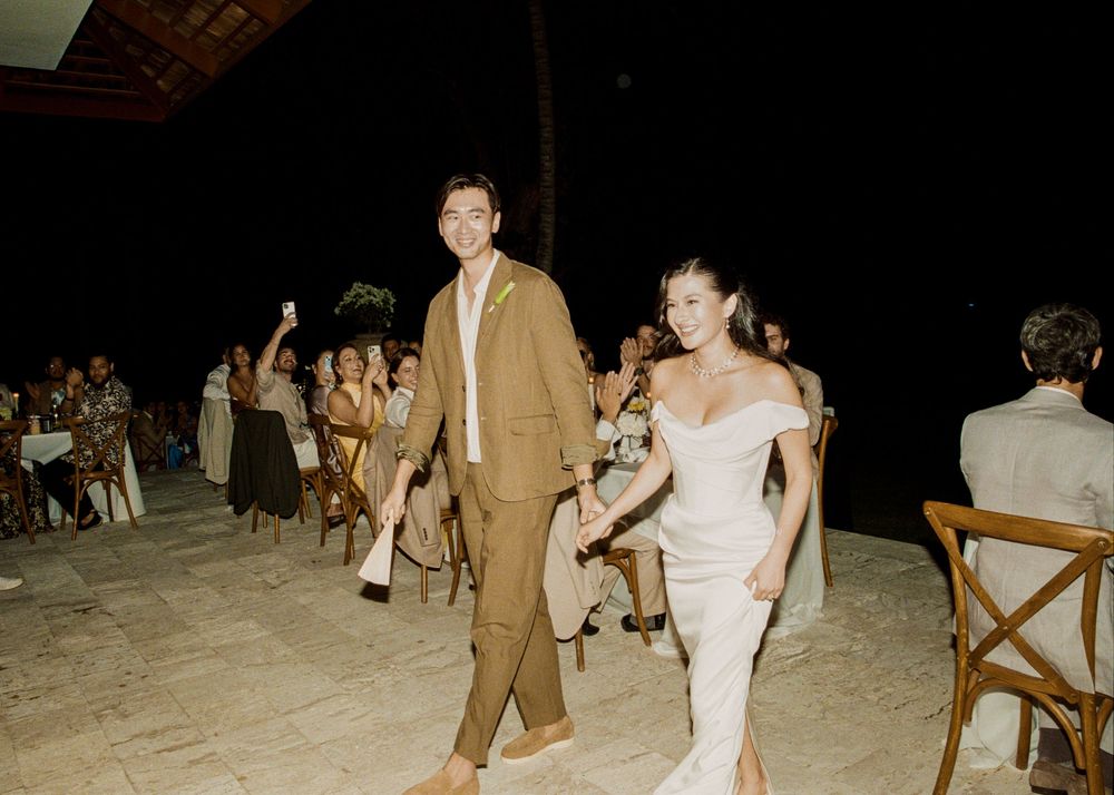 Evening beach wedding reception with guests seated at tables under dim lighting.