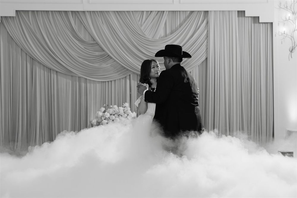 Black and white photo of a bride and groom sharing first dance surrounded by dramatic fog on a wedding reception dance floor.