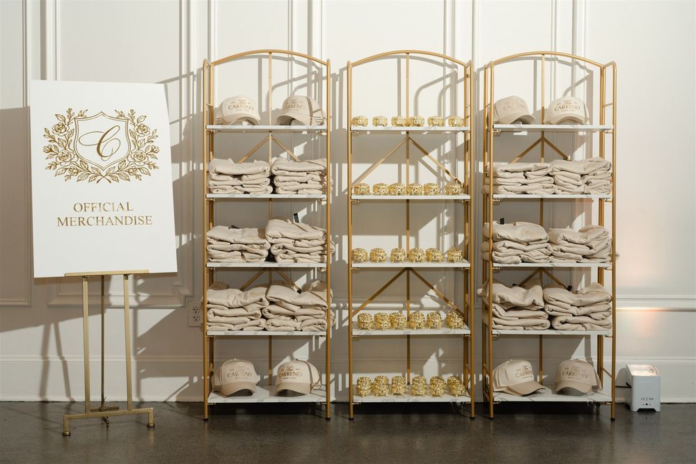 Gold shelving units displaying official merchandise including folded items and hats at an elegant event.
