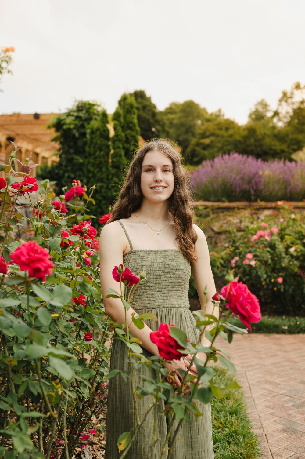 Young woman in green dress smiling among red roses in a beautiful garden.