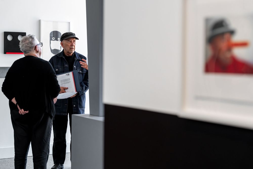 Two people conversing in an art gallery with framed photographs displayed on white walls.