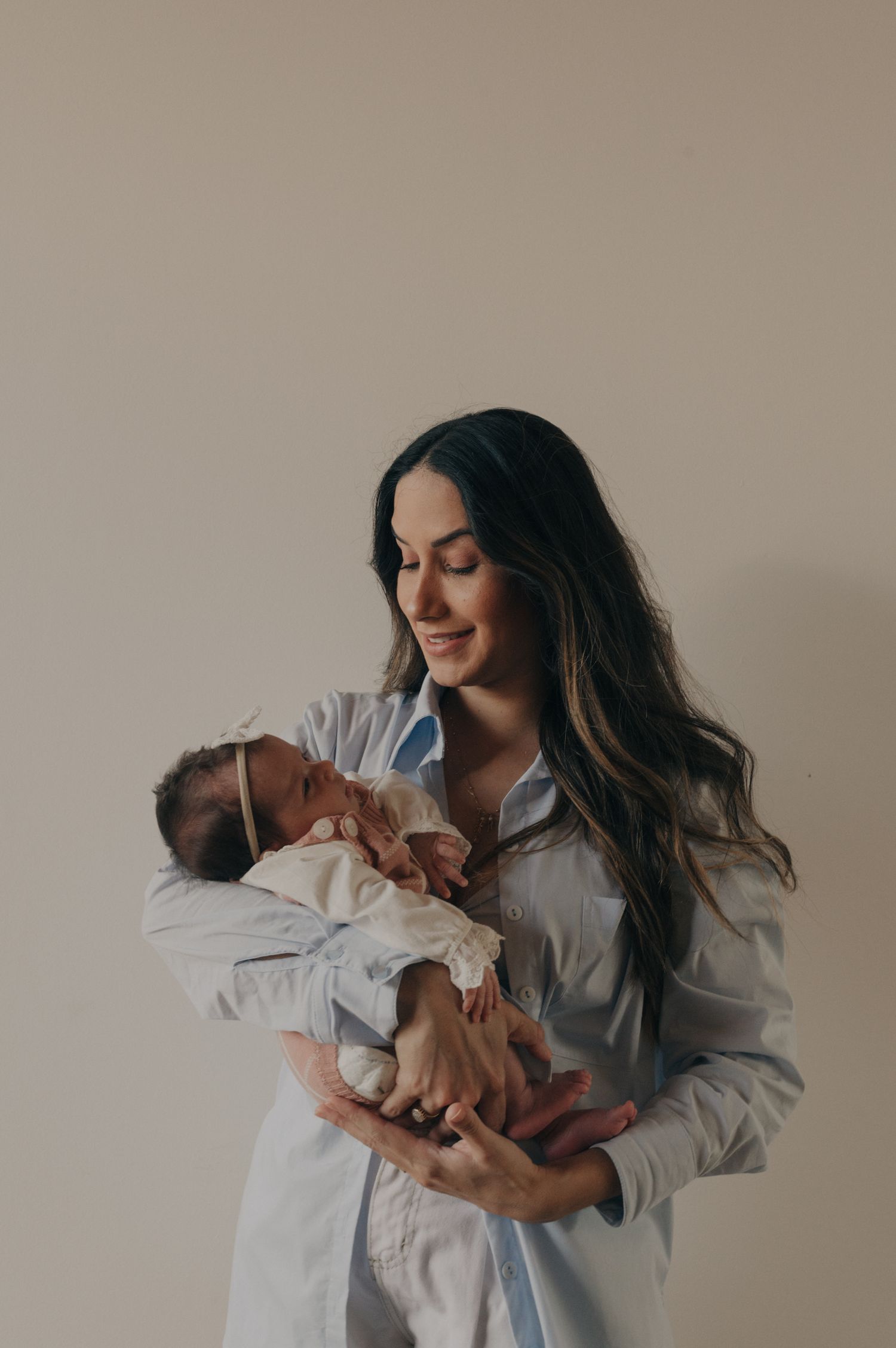 A gentle moment between parent and newborn in soft natural light against neutral background.