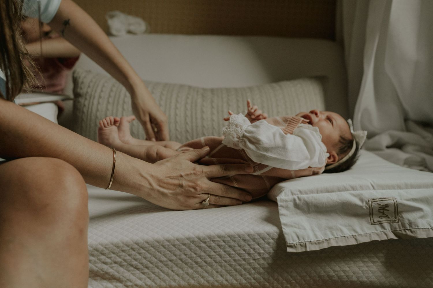 Gentle care moment with a newborn on textured bedding in warm ambient light.
