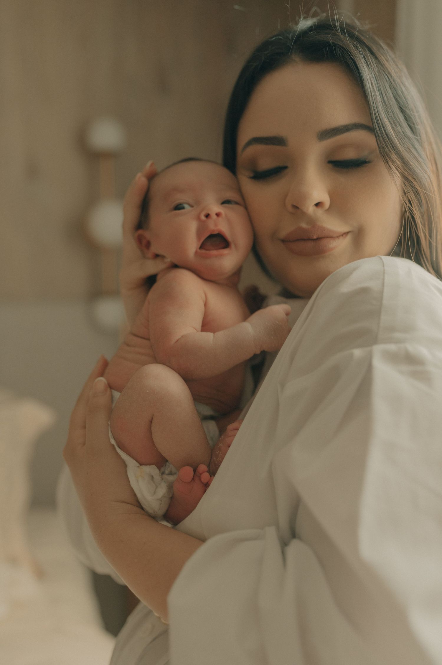 Intimate portrait of parent and baby sharing a loving embrace against neutral backdrop.
