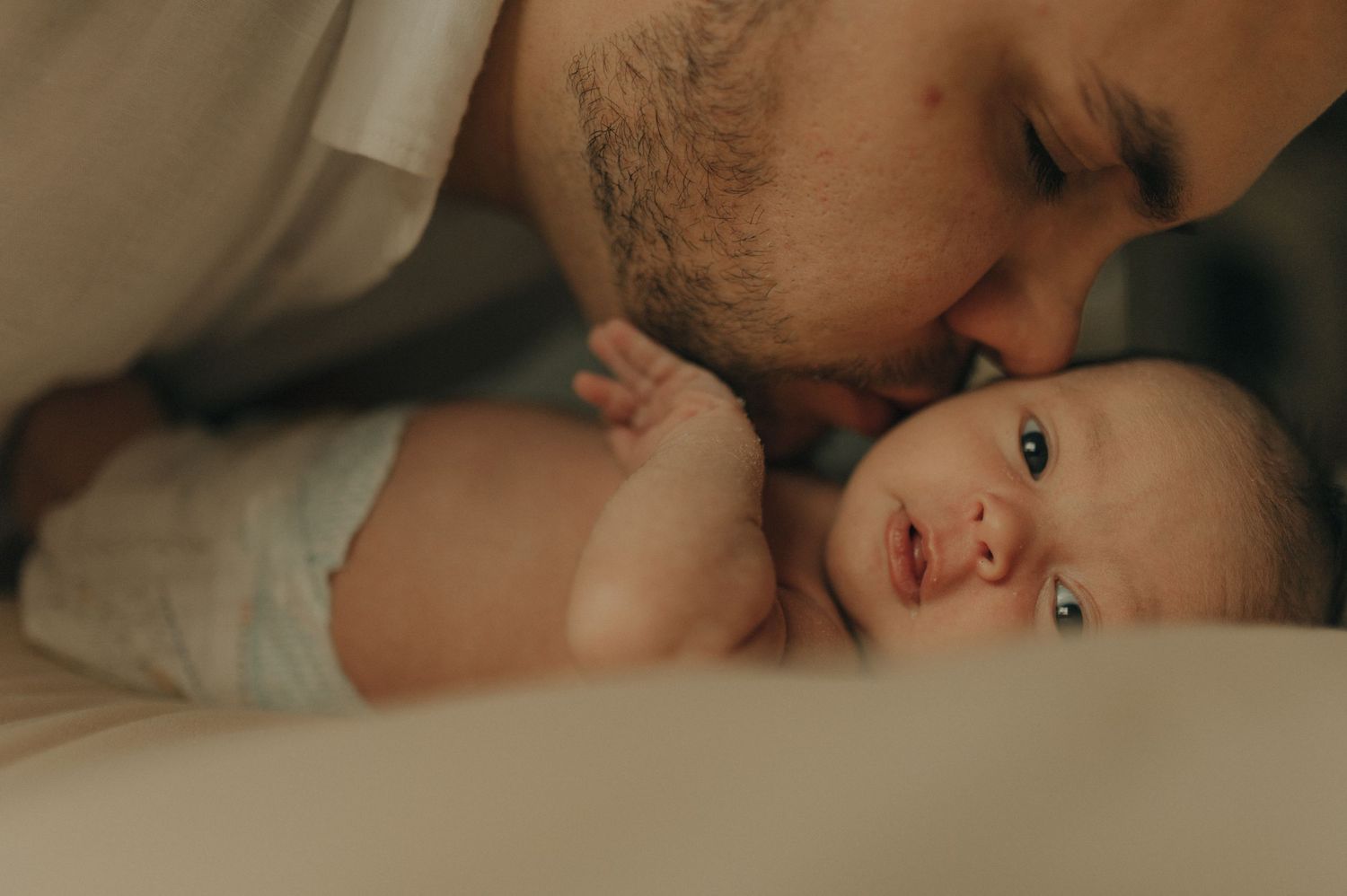 Tender moment between parent and infant in warm, intimate lighting.